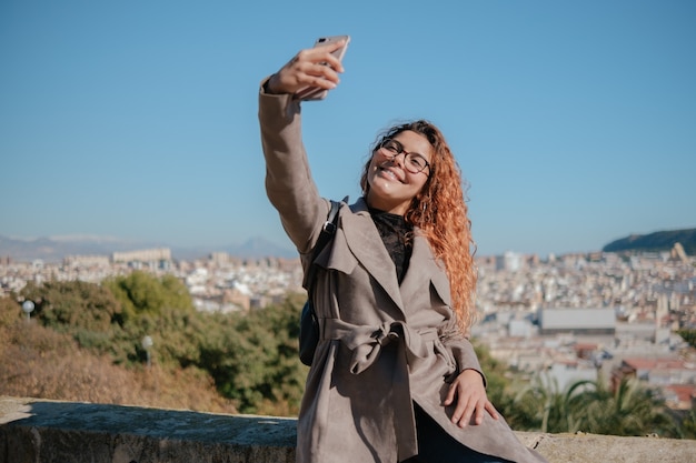 Photo pretty brunette latina girl doing a self portrait with her mobile phone outdoors