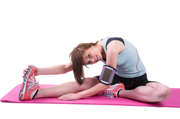 Pretty brunette looking at camera and stretching her leg on exercise mat