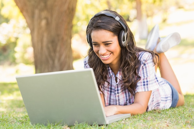 Pretty brunette lying in the grass and using laptop