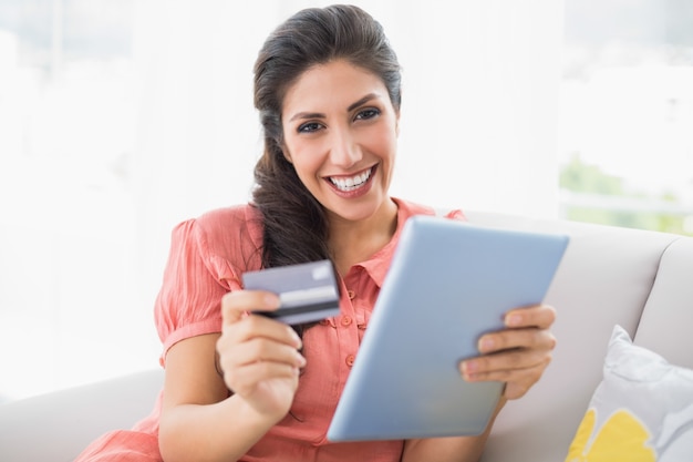 Pretty brunette sitting on her sofa using tablet to shop online