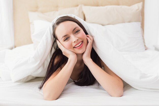 Pretty brunette smiling at camera in bed