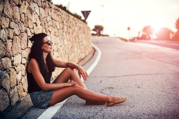 Милая брюнетка турист девушка сидит на дороге
