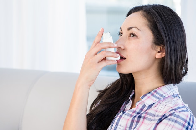 Pretty brunette using inhaler on couch