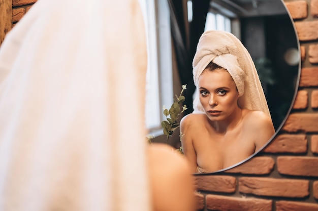 Pretty brunette with towel on her had standing near mirror in the bathroom after shower.