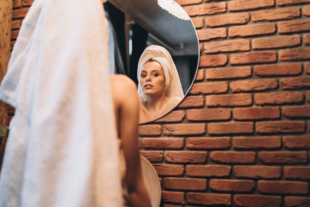 Photo pretty brunette with towel on her had standing near mirror in the bathroom after shower