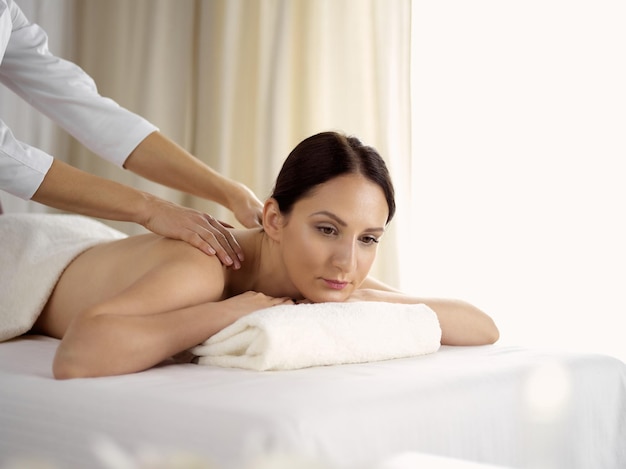 Pretty brunette woman enjoying procedure of back massage in spa salon. Beauty concept.