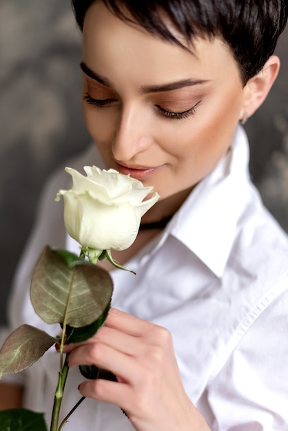 Pretty brunette woman holds white rose in her hand close up portrait.