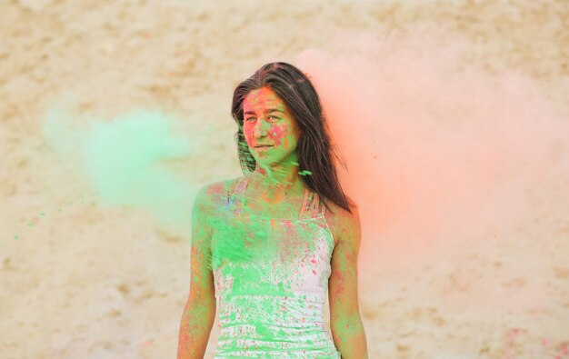 Pretty brunette woman posing with exploding green and orange dry Holi powder at the desert