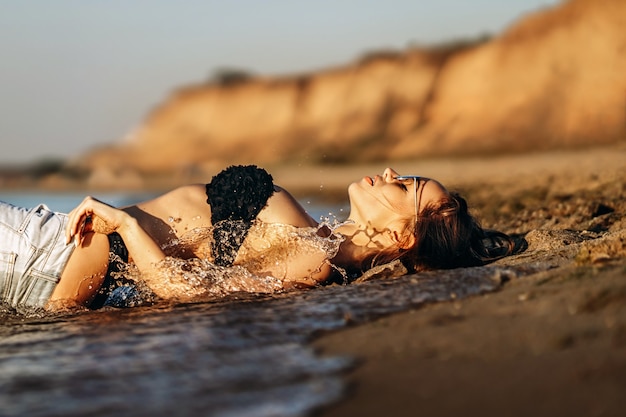 Donna graziosa del brunette che si distende sulla spiaggia al mare.