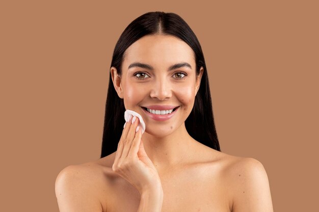 Pretty brunette woman touching her face with cotton pad closeup