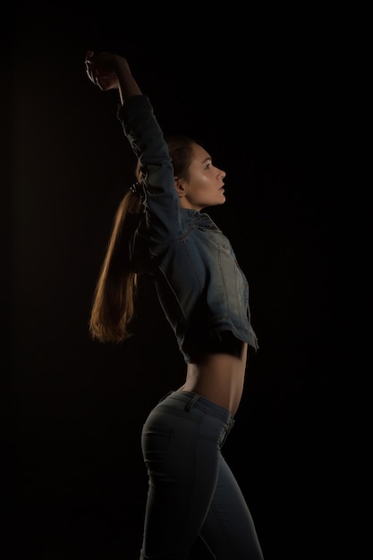 Pretty brunette woman in trendy jeans jacket posing at black background