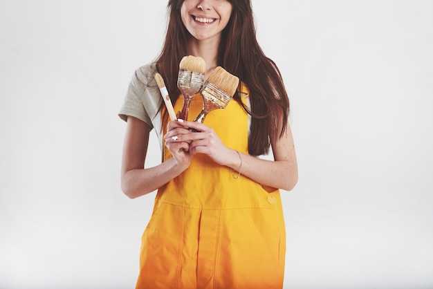 Pretty brunette woman in yellow uniform stands against white wall