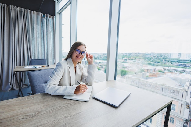 Bella donna d'affari che guarda attraverso il taccuino concentrato sul lavoro libero professionista lavoro a distanza studio studio moderno ufficio interno distanza sociale donna in ufficio con occhiali e laptop