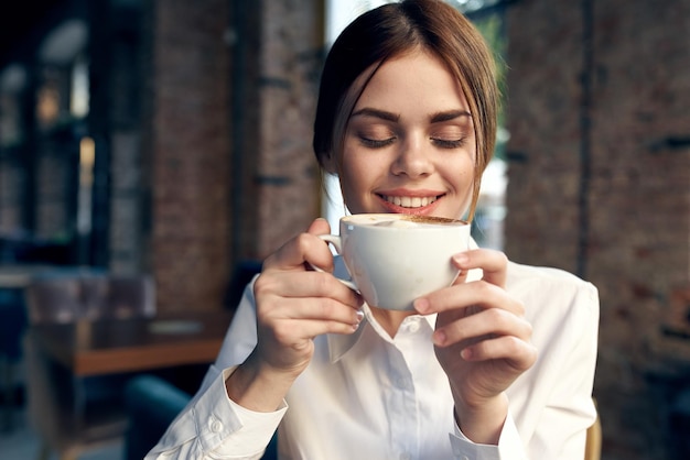 Photo pretty business woman in white shirt sits in a cafe with a cup of coffee high quality photo