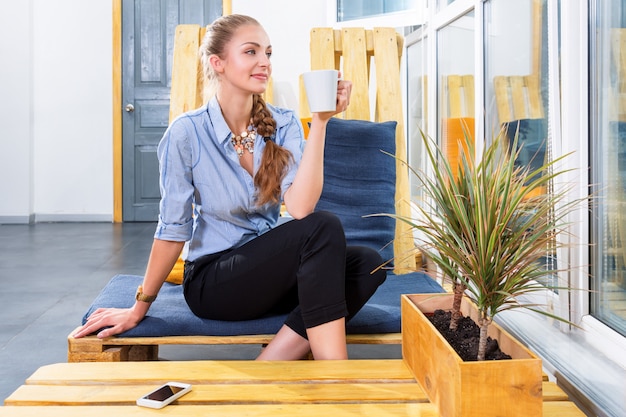 Pretty businesswoman drinking hot morning coffee and dreaming in modern loft. Woman in businness. Freelancer in coworking center is resting and enjoying the drink. Freelance work concept.