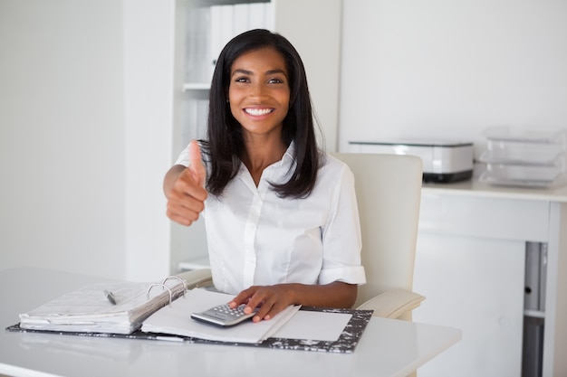 Pretty businesswoman showing thumb up to camera at her desk