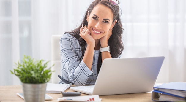 Pretty businesswoman smiles at the camera while sitting at her desk in front of the computer.