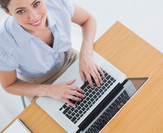 Pretty businesswoman typing on her laptop and smiling up at camera