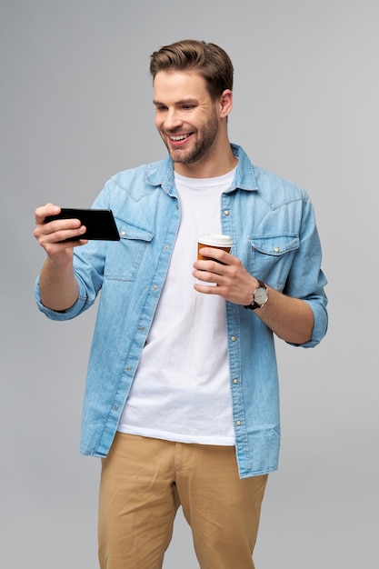 pretty casual man in blue jeans shirt holding his phone and cup of coffee to go