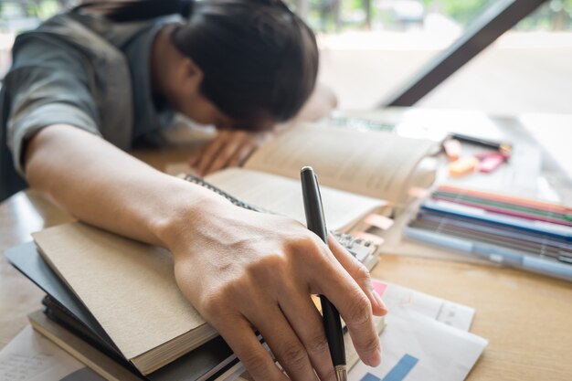 Ragazza abbastanza caucasica che dorme sul suo libro vicino a un mucchio di libri