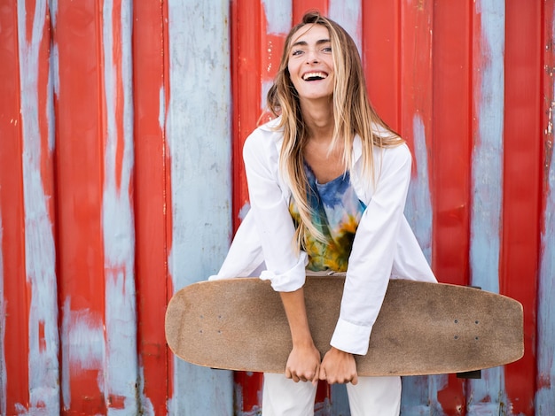 Foto donna abbastanza caucasica skater sorridente e in piedi su uno sfondo rosso