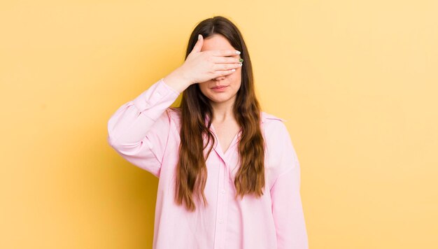 片手で目を覆っているかなり白人の女性は、怖い、不安を感じている、または盲目的に驚きを待っている