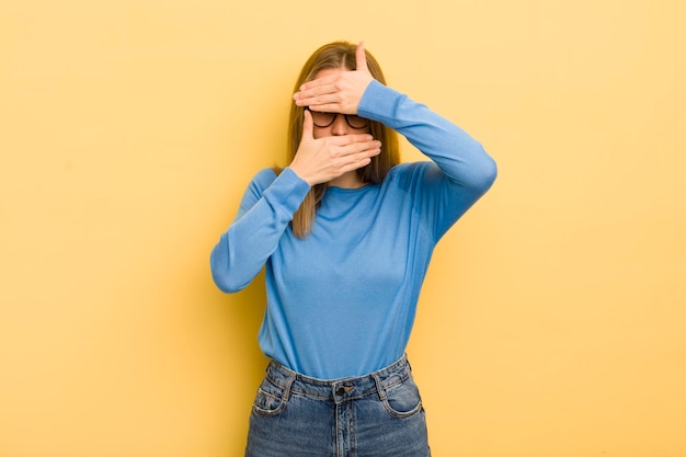 Pretty caucasian woman covering face with both hands saying no\
to the camera refusing pictures or forbidding photos