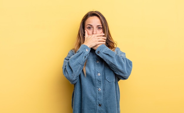 Pretty caucasian woman covering mouth with hands with a shocked, surprised expression, keeping a secret or saying oops