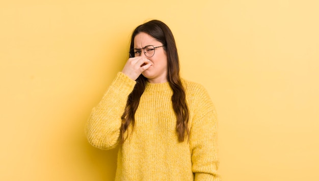 Pretty caucasian woman feeling disgusted holding nose to avoid smelling a foul and unpleasant stench