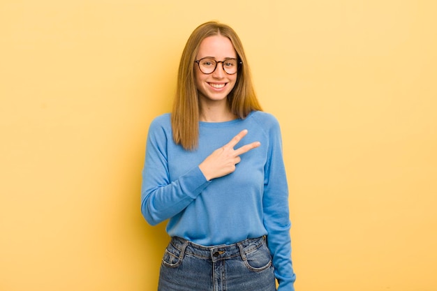 Pretty caucasian woman feeling happy positive and successful with hand making v shape over chest showing victory or peace