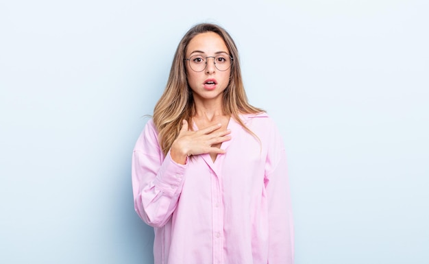 Pretty caucasian woman feeling shocked, astonished and surprised, with hand on chest and open mouth, saying who, me?