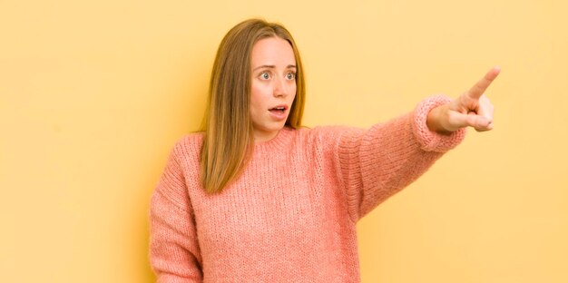 Donna abbastanza caucasica che si sente scioccata e sorpresa indicando e guardando verso l'alto con stupore con uno sguardo stupito a bocca aperta