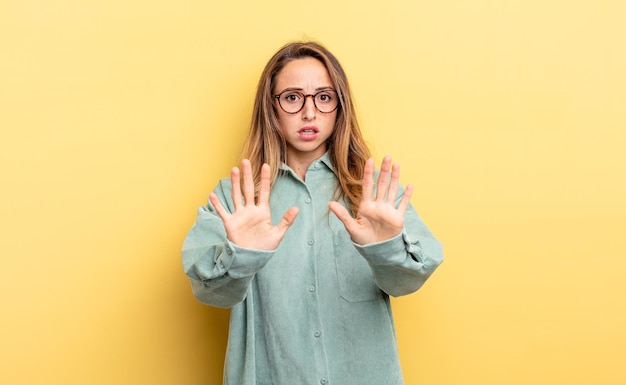 Pretty caucasian woman feeling stupefied and scared, fearing something frightening, with hands open up front saying stay away