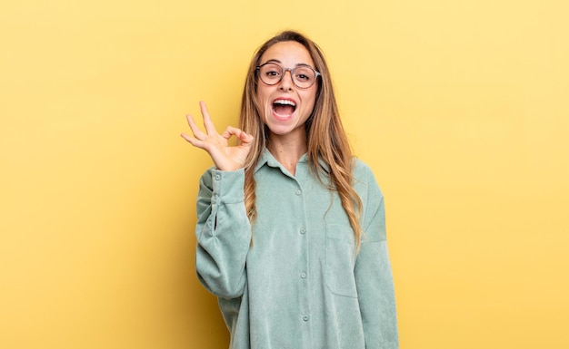 Pretty caucasian woman feeling successful and satisfied, smiling with mouth wide open, making okay sign with hand