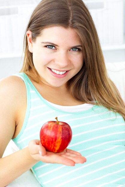 Pretty caucasian woman holding an apple sitting on a sofa