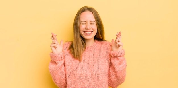 Pretty caucasian woman smiling and anxiously crossing both fingers feeling worried and wishing or hoping for good luck