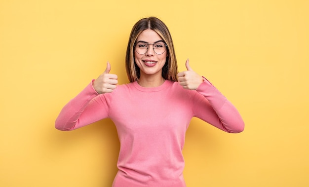 Pretty caucasian woman smiling broadly looking happy, positive, confident and successful, with both thumbs up