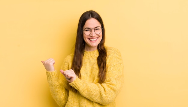 Pretty caucasian woman smiling cheerfully and casually pointing to copy space on the side feeling happy and satisfied