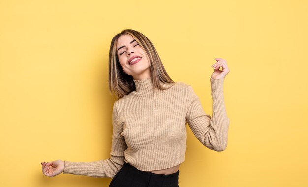 Pretty caucasian woman smiling, feeling carefree, relaxed and happy, dancing and listening to music, having fun at a party