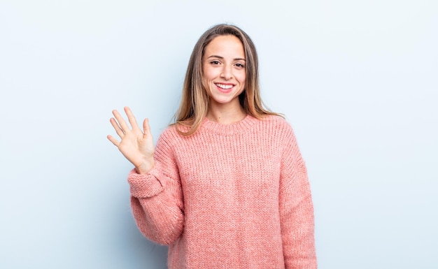 Pretty caucasian woman smiling happily and cheerfully, waving hand, welcoming and greeting you, or saying goodbye
