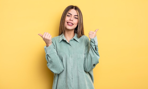 Pretty caucasian woman smiling joyfully and looking happy, feeling carefree and positive with both thumbs up