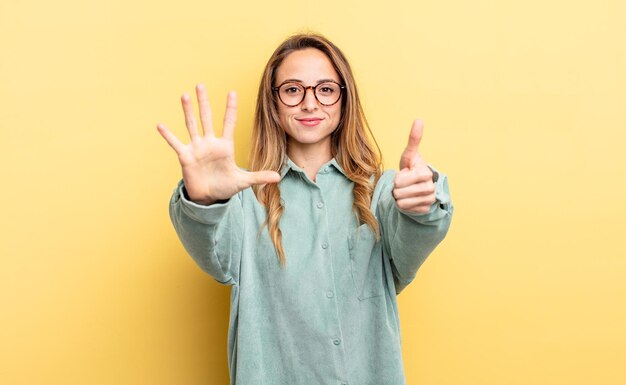 pretty caucasian woman smiling and looking friendly, showing number six or sixth with hand forward, counting down