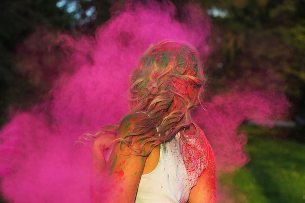 Pretty caucasian woman with curly hair posing in a cloud of pink dry paint, celebrating Holi festival