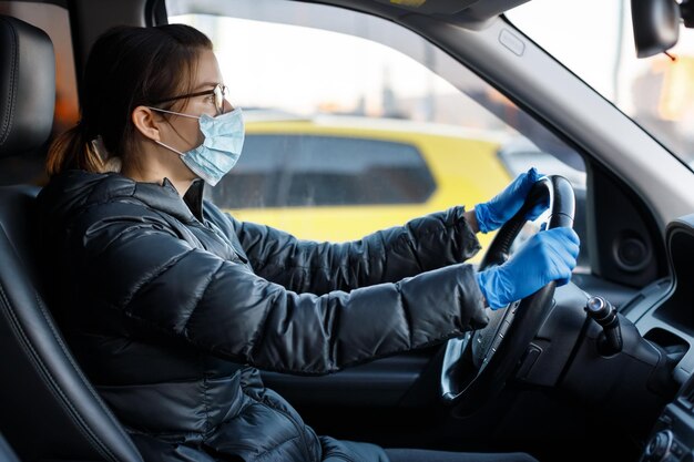 Pretty caucasian woman with glasses anti virus medical mask and blue latex gloves driving a car