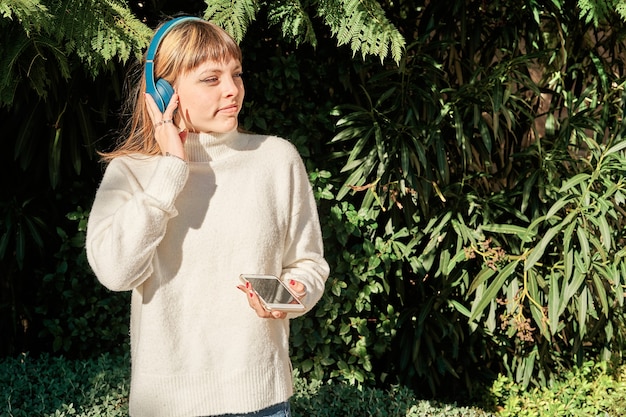 Довольно кавказская молодая девушка слушает музыку с синими наушниками в парке