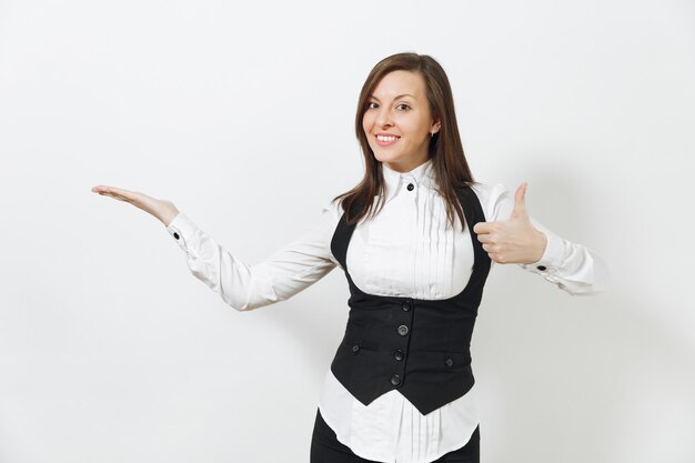 Pretty caucasian young smiling brown-hair business woman in black suit, white shirt, pointing hand aside, showing thumb up isolated on white wall