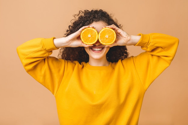 Photo pretty charming joyful attractive cheerful funny comic positive curly girl having two pieces of orange, isolated on beige