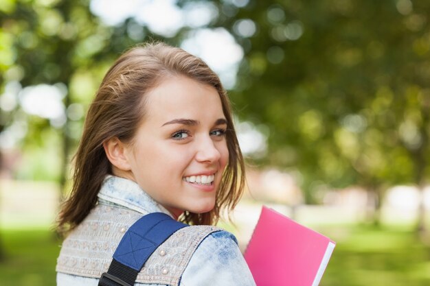 Pretty cheerful student smiling at camera carrying notebook