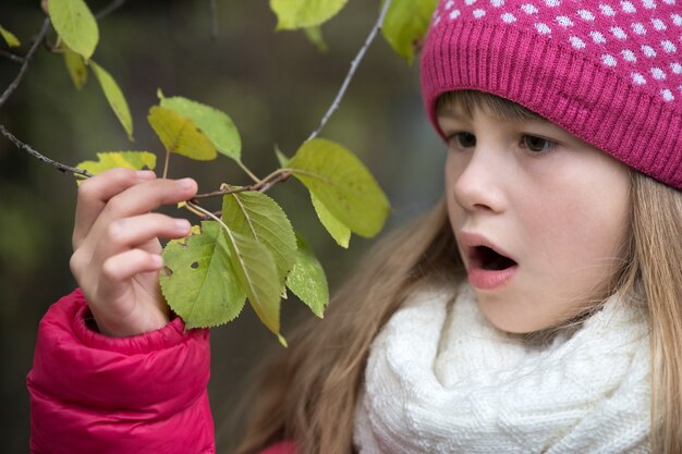 Pretty child girl holding tree branch with green leaves.