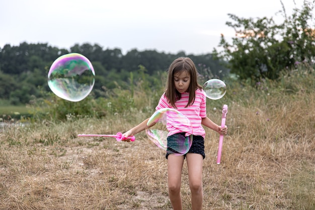 Una graziosa bambina lancia enormi bolle di sapone sullo sfondo della bellissima natura. Foto Premium